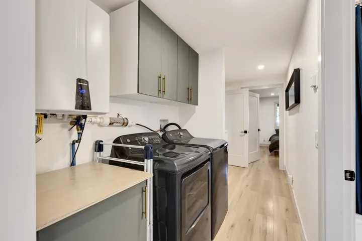 Laundry room with light wood-style floors, tankless water heater, cabinet space, independent washer and dryer, and recessed lighting