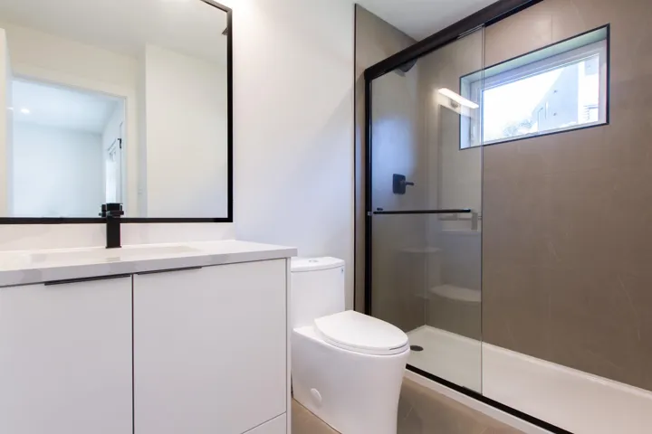 Bathroom with tiled shower, toilet, and vanity