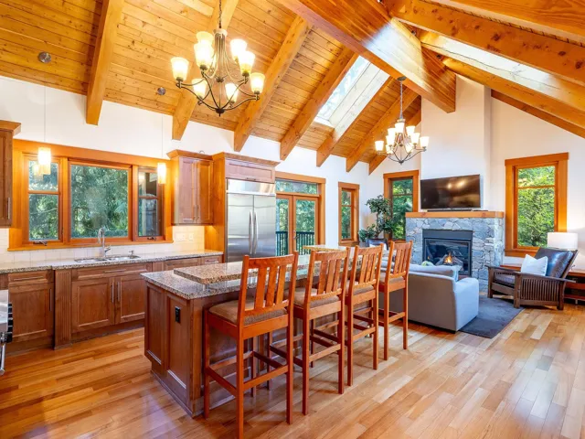 Dining area featuring a chandelier, a stone fireplace, light wood finished floors, high vaulted ceiling, and a skylight