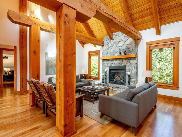 Living area with a stone fireplace, light wood-style floors, a wood ceiling with exposed beams, and high vaulted ceiling