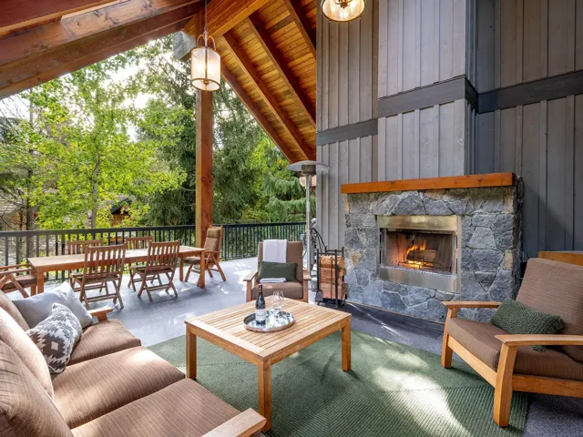 Living room with an outdoor stone fireplace, floor to ceiling windows, view of wooded area, and wood ceiling