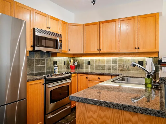 Kitchen featuring dark stone counters, a sink, backsplash, and stainless steel appliances