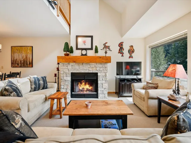 Living area with light carpet, high vaulted ceiling, and a stone fireplace