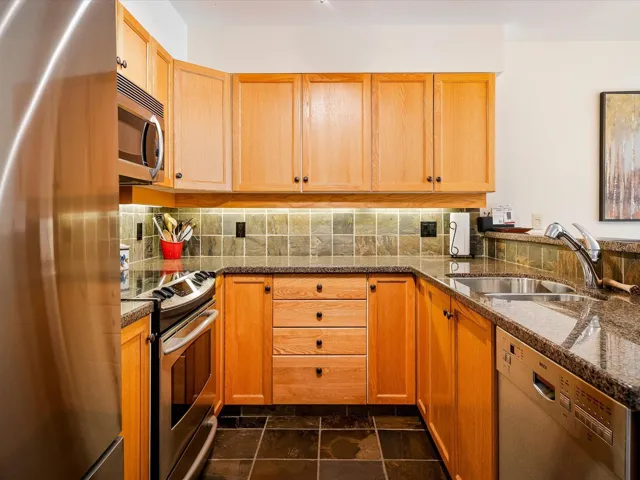 Kitchen featuring appliances with stainless steel finishes, dark stone countertops, a peninsula, decorative backsplash, and a sink