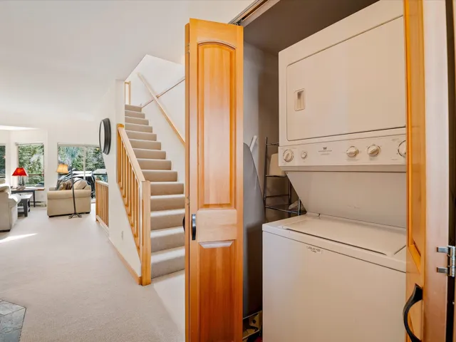Laundry room with stacked washer / dryer, laundry area, and light carpet