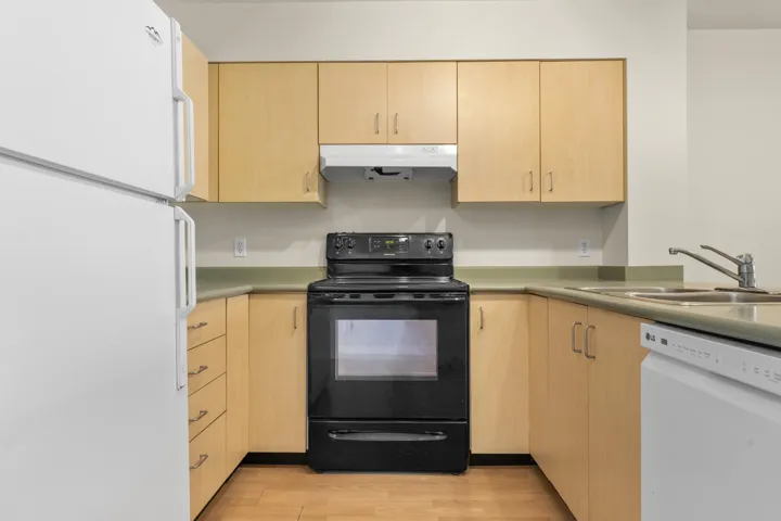 Kitchen with white appliances, light brown cabinets, a sink, and under cabinet range hood