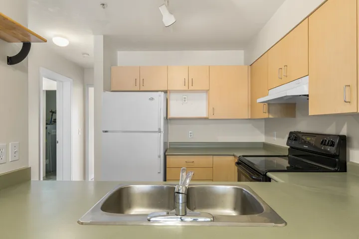 Kitchen featuring light brown cabinetry, freestanding refrigerator, a sink, black range with electric cooktop, and under cabinet range hood