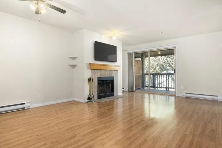 Unfurnished living room featuring a baseboard heating unit, a tile fireplace, baseboards, and light wood finished floors