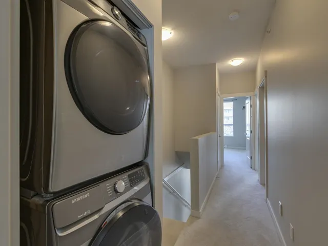 Laundry area featuring stacked washer / dryer and light colored carpet