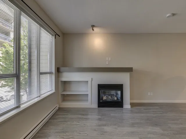 Unfurnished living room with baseboard heating, wood finished floors, and a glass covered fireplace