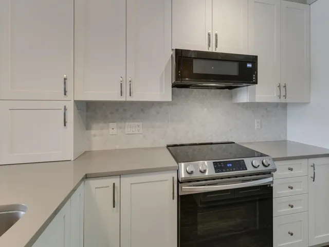 Kitchen with stainless steel electric range, white cabinets, black microwave, and tasteful backsplash