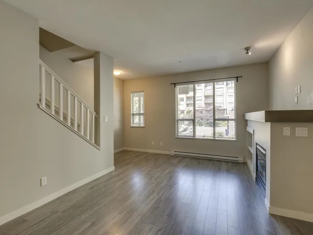 Unfurnished living room with dark wood-style floors, baseboard heating, a glass covered fireplace, and a textured ceiling