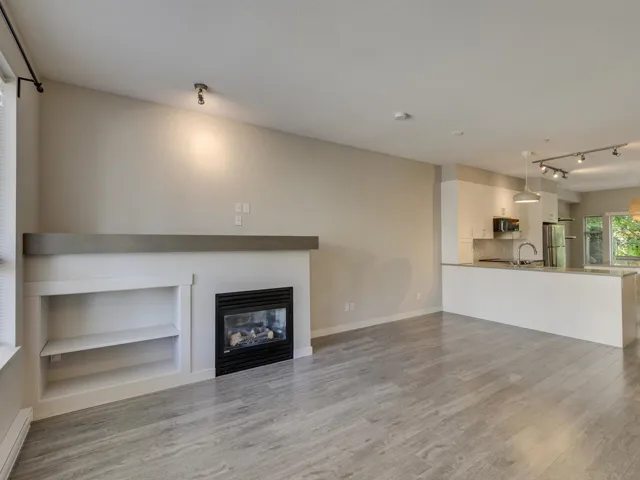 Unfurnished living room featuring light wood-style floors, rail lighting, a glass covered fireplace, and a baseboard radiator