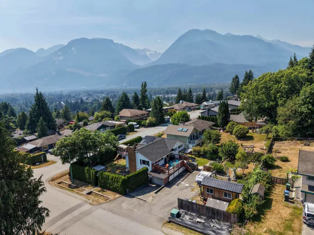 Aerial perspective of a neighborhood featuring homes with varied architectural styles and mature landscaping, framed by distant mountain ranges