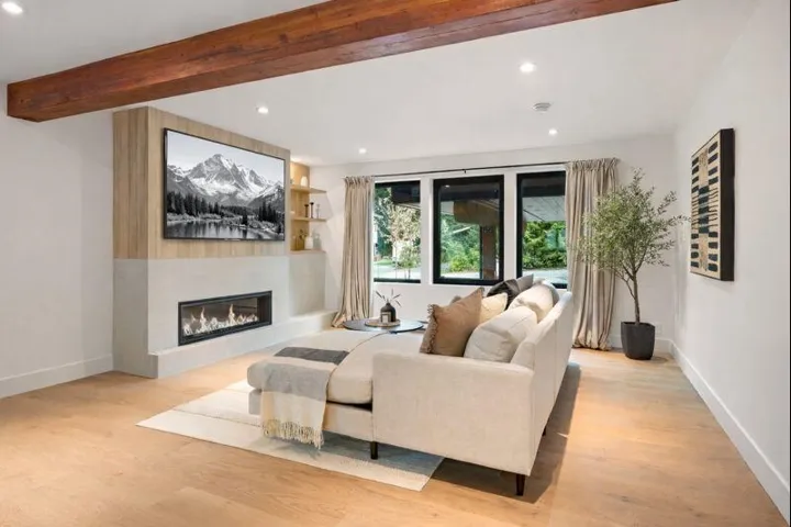 Living area with light wood-style floors, a glass covered fireplace, beamed ceiling, and recessed lighting