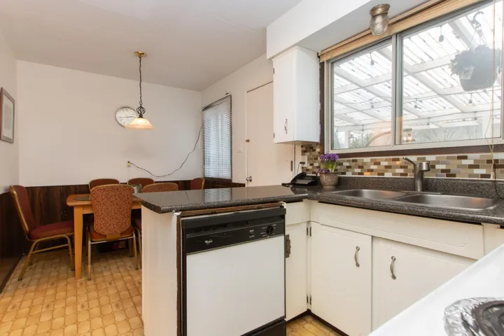 Kitchen featuring dark countertops, white dishwasher, a sink, light floors, and white cabinetry