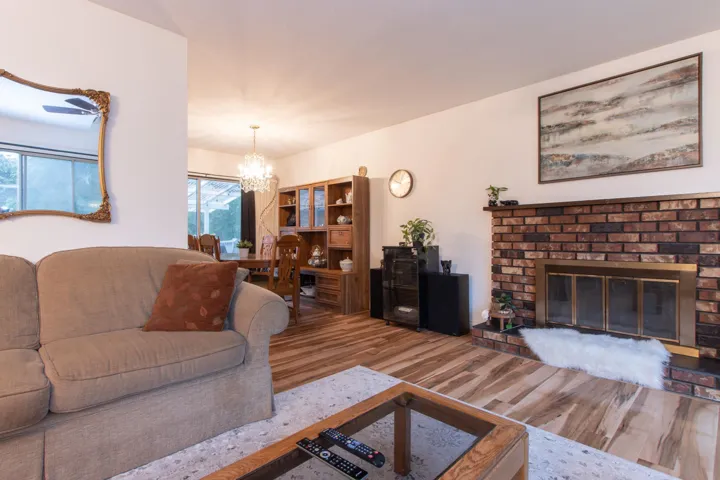 Living room with a notable chandelier, a brick fireplace, and wood finished floors
