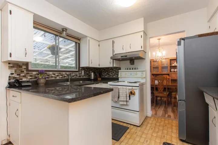 Kitchen featuring under cabinet range hood, light floors, electric stove, a sink, and freestanding refrigerator