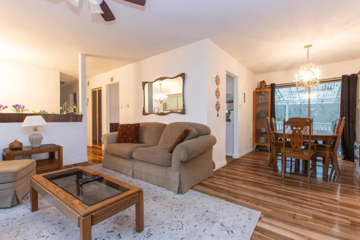 Living room with ceiling fan with notable chandelier, baseboards, and wood finished floors