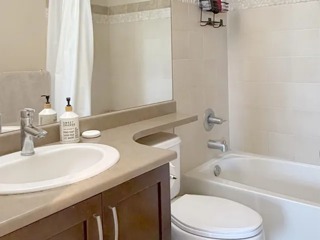 Bathroom featuring an integrated countertop sink, dark wood-finish vanity, large wall mirror, white bathtub, and light-toned tile surround with decorative accent border