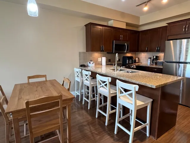 Open-concept kitchen featuring rich wood cabinetry, stainless steel appliances, granite countertops, and a tile backsplash