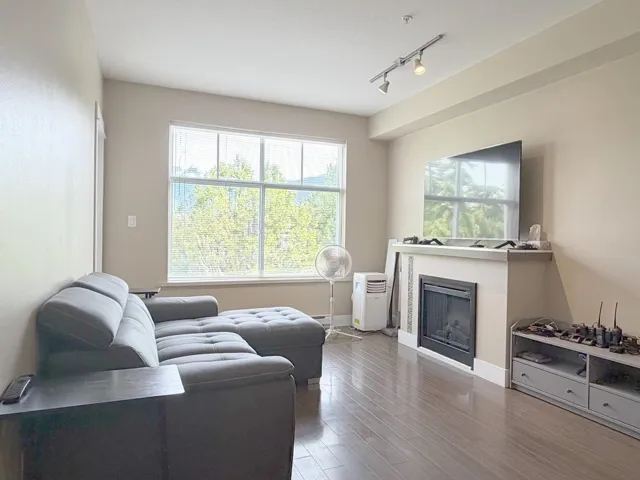 Living area featuring wood-finish flooring, a large window, fireplace with mantel, and track lighting