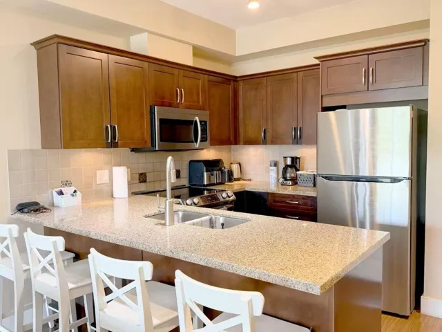 Kitchen featuring wood-finish cabinetry, stainless steel appliances, a tile backsplash, recessed lighting, and a peninsula with a double basin sink