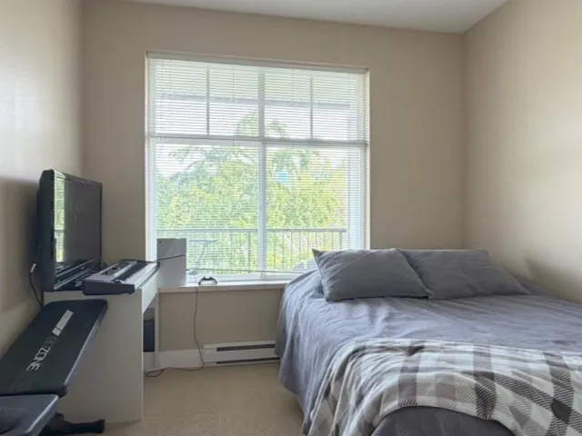 Bright bedroom featuring a large window with horizontal blinds, neutral wall paint, and beige carpet flooring