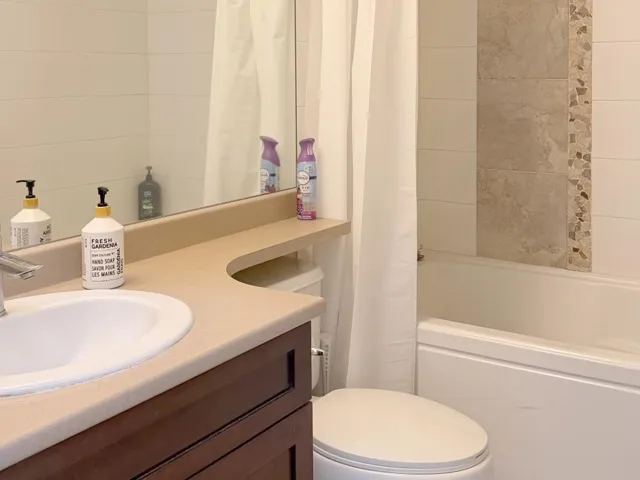 Bathroom featuring a built-in bathtub, a vanity with a drop-in sink, a built-in toilet, and a tiled shower surround with an accent strip