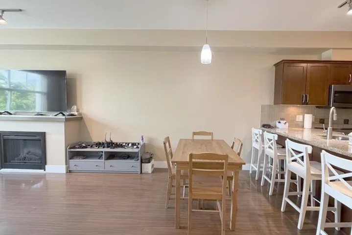 Open-concept living space featuring wood-finish flooring, a fireplace with a mantel, and a kitchen island with seating
