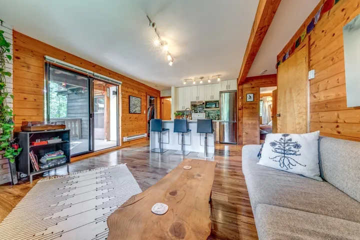 Living area featuring rail lighting, wooden walls, light wood finished floors, and a baseboard heating unit