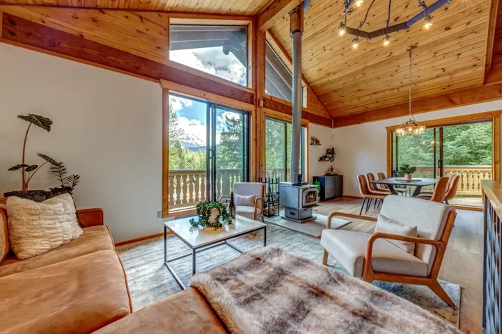 Living area featuring a wood stove, healthy amount of natural light, wood ceiling, a chandelier, and high vaulted ceiling