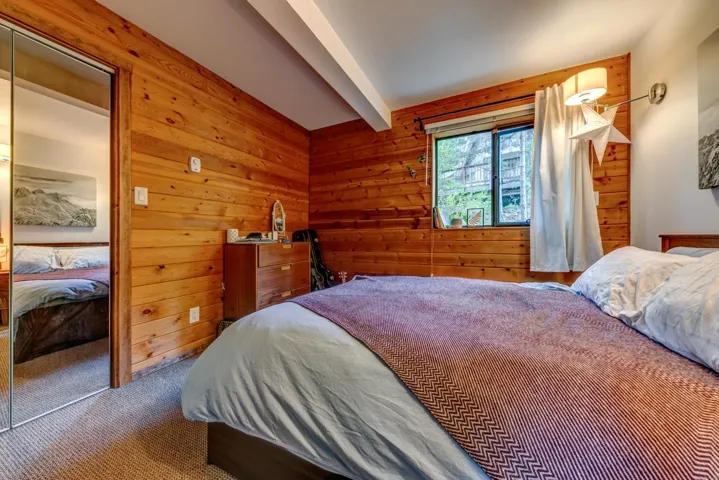 Bedroom with wooden walls, carpet, and beam ceiling