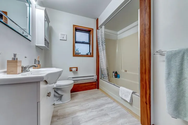 Full bath with baseboard heating, toilet, wood finished floors, vanity, and shower / tub combo