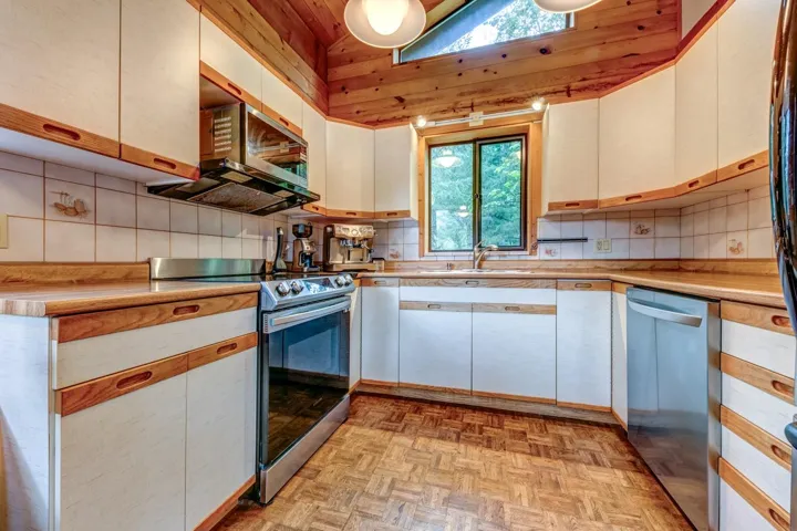 Kitchen featuring stainless steel appliances, a sink, light countertops, backsplash, and high vaulted ceiling