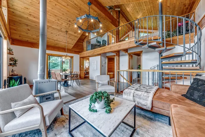 Living area with a chandelier, high vaulted ceiling, wooden ceiling, wood finished floors, and a wood stove