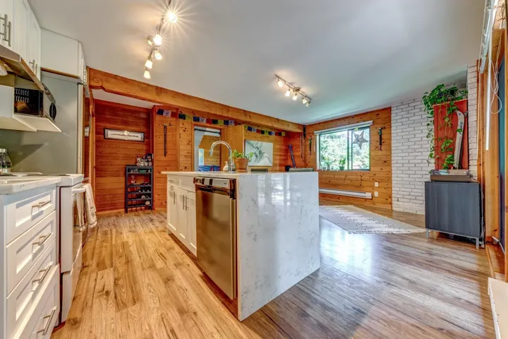 Kitchen with electric range oven, rail lighting, stainless steel dishwasher, light countertops, and light wood finished floors