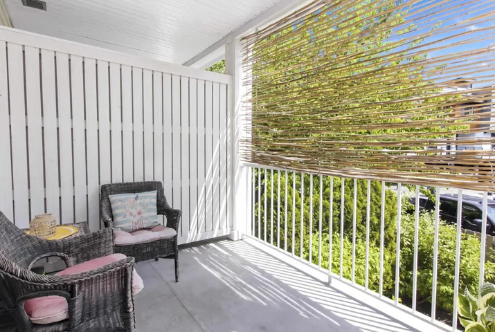 Covered patio featuring a white slatted privacy wall, concrete flooring, and a bamboo screen