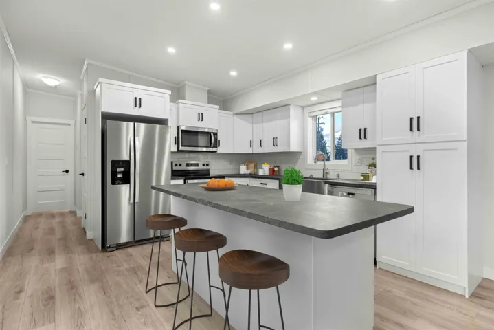 Kitchen featuring white shaker-style cabinetry, matte black hardware, a dark-toned island countertop, stainless steel appliances, and wood-finish flooring