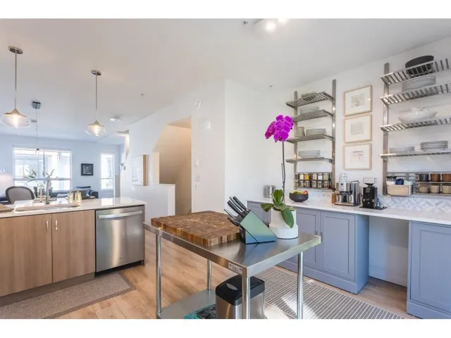Kitchen with light wood finished floors, stainless steel dishwasher, light stone counters, pendant lighting, and open floor plan