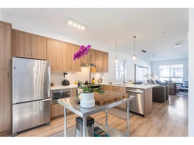 Kitchen with stainless steel appliances, decorative light fixtures, open floor plan, light wood-style flooring, and a peninsula
