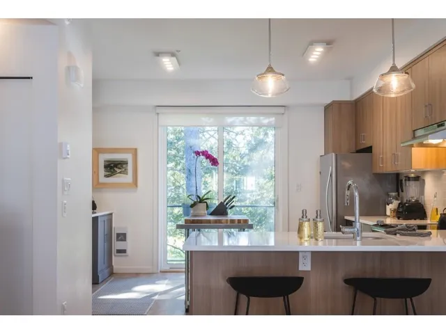 Kitchen featuring wood finish cabinets, modern cabinets, freestanding refrigerator, a peninsula, and decorative light fixtures