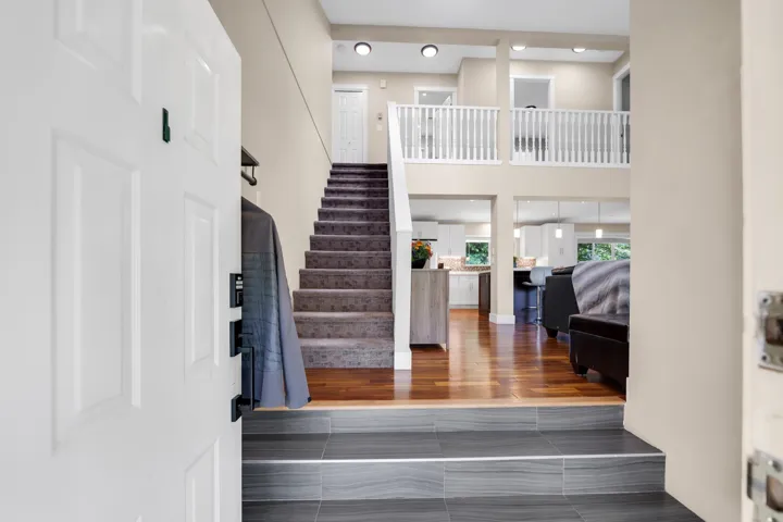 Multi-level entryway featuring dark gray tile flooring and a carpeted staircase leading to an upper landing with white balusters