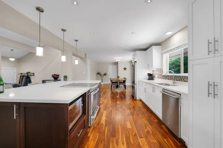 Kitchen featuring wood-finish flooring, white cabinetry, a large island with white countertops and pendant lighting, stainless steel appliances, and a mosaic tile backsplash