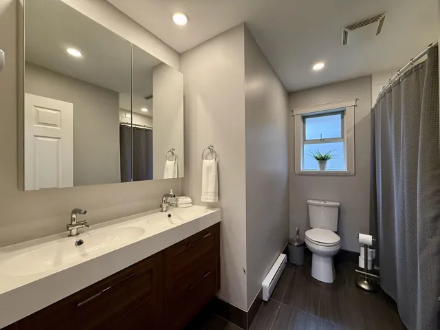 Full bath featuring double vanity, recessed lighting, baseboard heating, and curtained shower