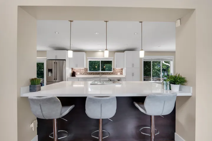 Kitchen pass-through featuring a white countertop breakfast bar with three pendant lights