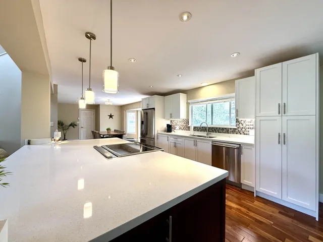 Kitchen with white cabinetry, dark wood-style floors, decorative light fixtures, stainless steel appliances, and tasteful backsplash