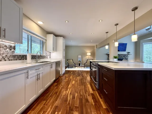 Dual tone kitchen with stainless steel appliances, dark wood-style flooring, two tone cabinets, hanging light fixtures, and plenty of natural light