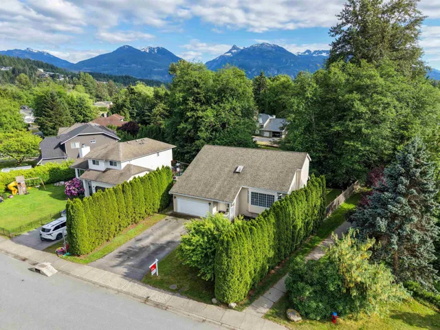 Residential property featuring a light-toned exterior with a dark shingle roof, surrounded by mature trees and lush green landscaping