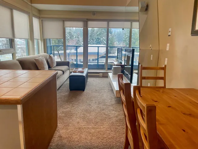 Living area with dark colored carpet, a wall mounted air conditioner, and a baseboard radiator